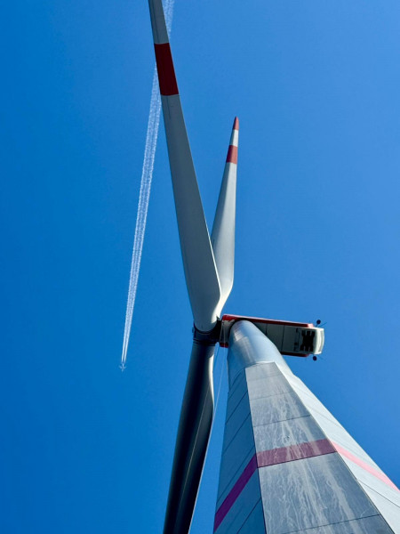 Eine Windenergieanlage aus der Froschperspektive. Weit oberhalb zieht ein Flugzeug Kondensstreifen am blauen Himmel.