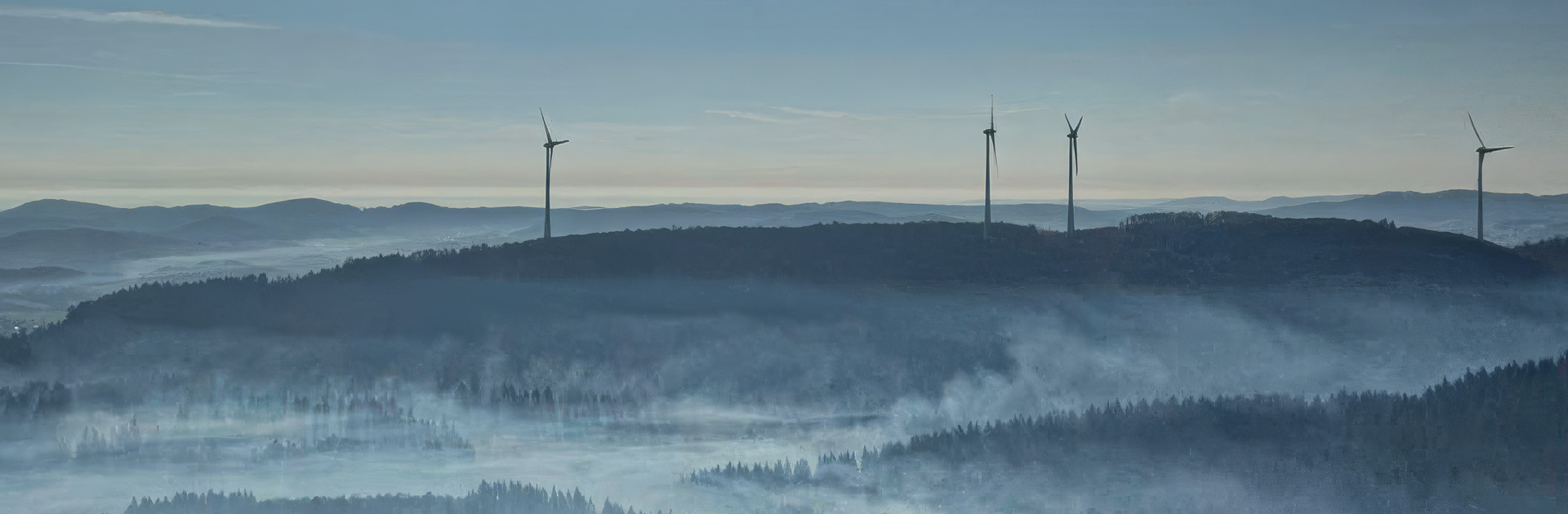 Windräder stehen in der Morgendämmerung auf einem dunklen Bergrücken.
